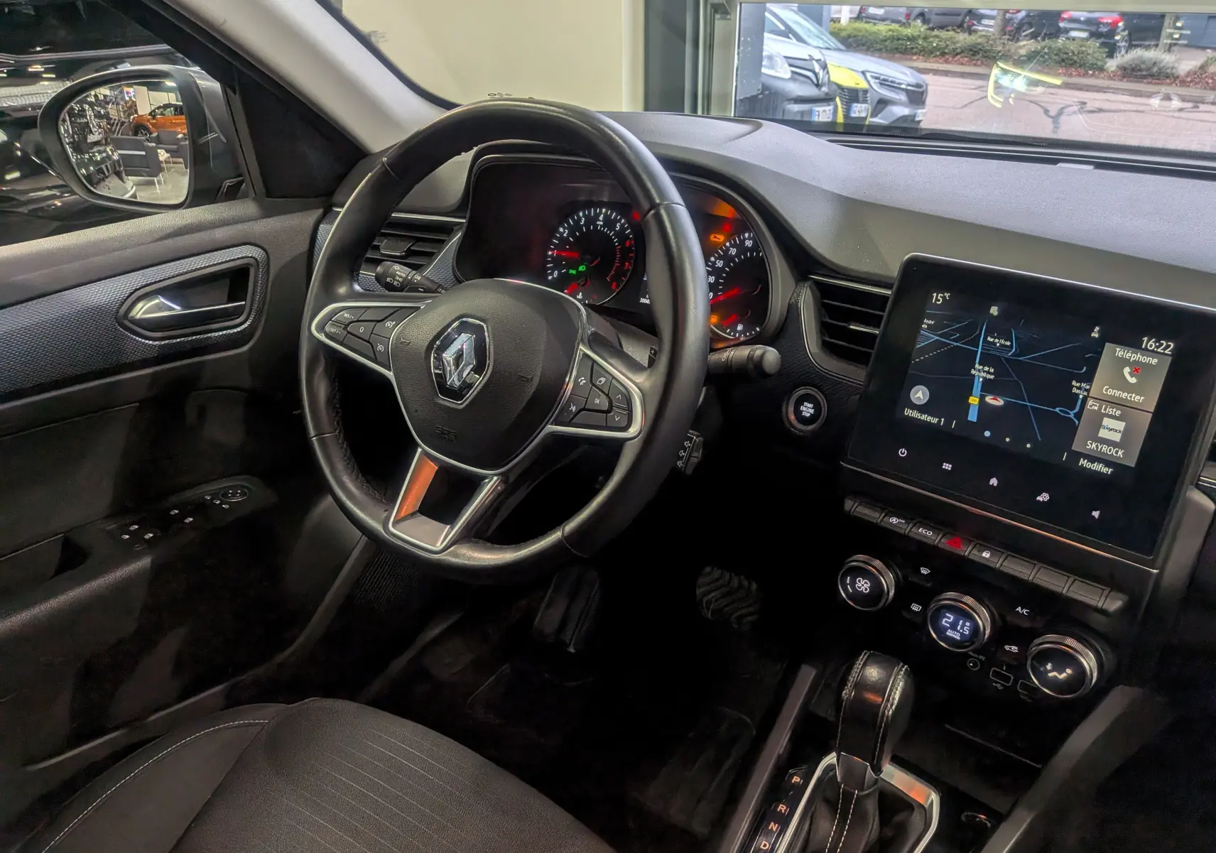 Vue intérieure côté conducteur du Renault Arkana gris métal 2022, avec volant multifonction et écran tactile central allumé.