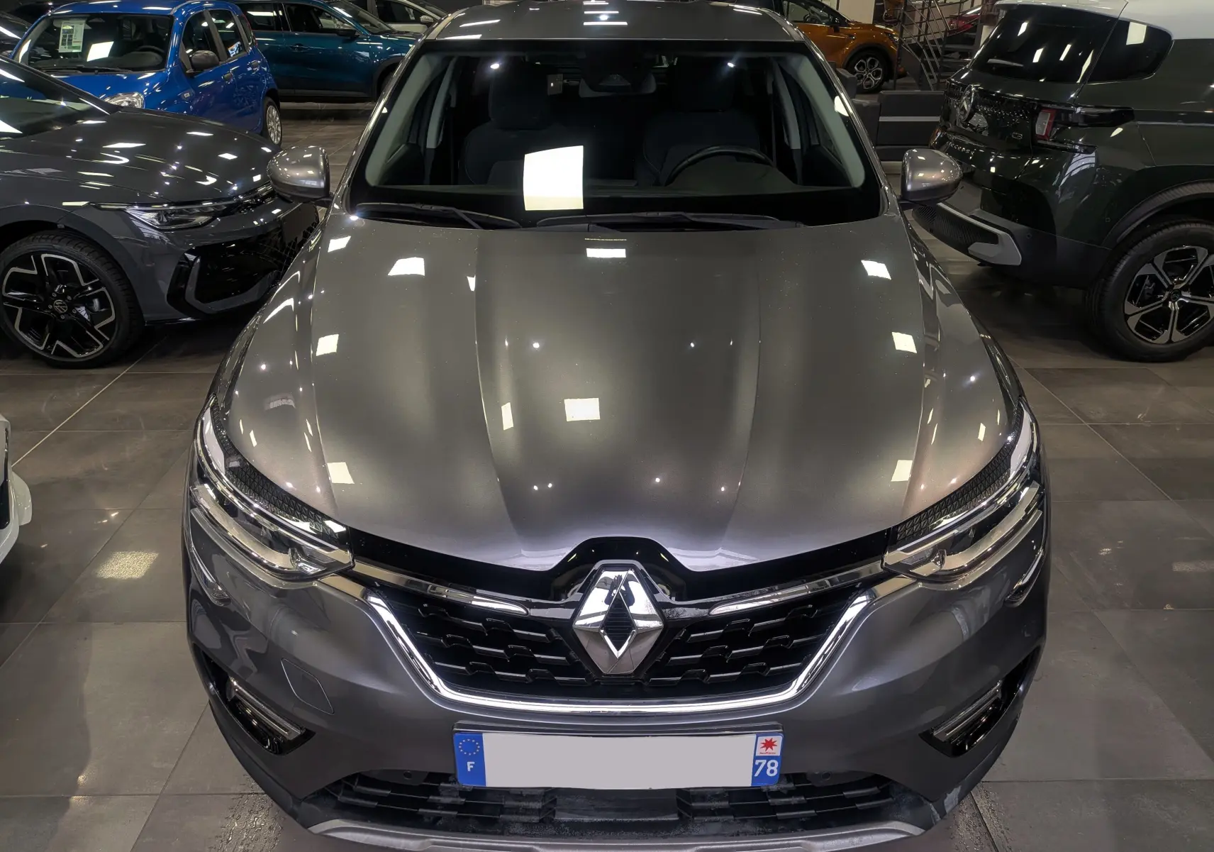 Vue avant plongeante d'un Renault Arkana TCe 140 Business gris métal, avec calandre chromée et logo Renault bien visible.