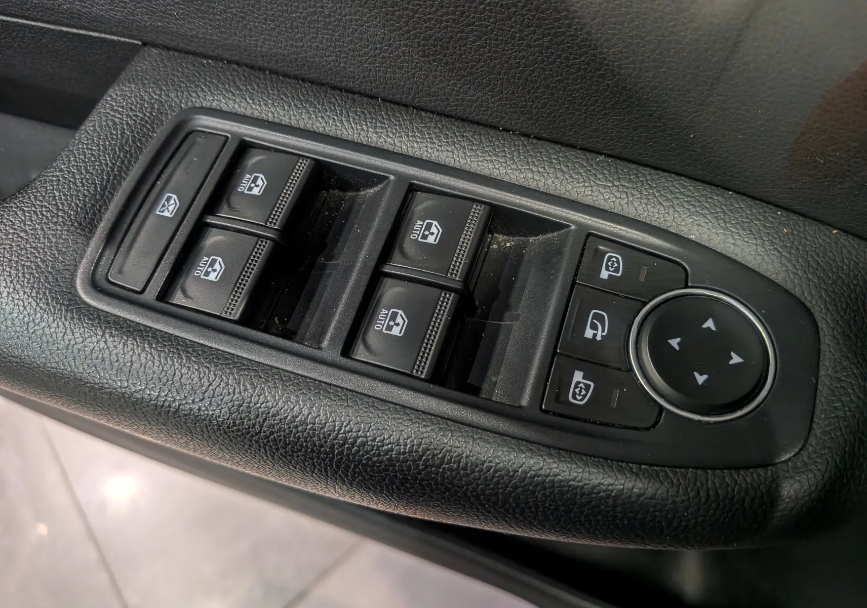 Gros plan sur les commandes de lève-vitres et réglages des rétroviseurs côté conducteur d’un Renault Arkana gris métal.