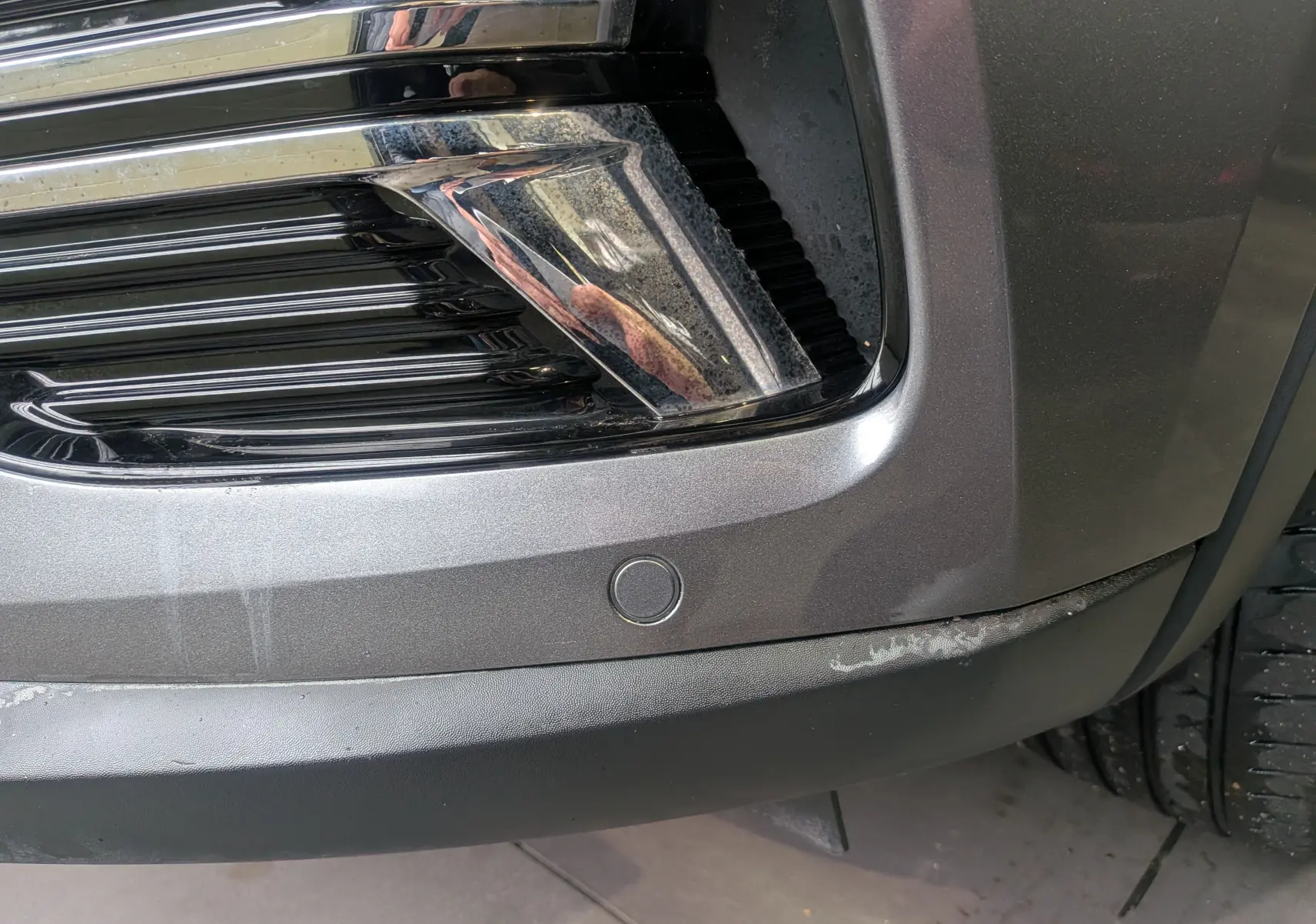 Gros plan sur le pare-chocs avant gris métal du Renault Arkana TCe 140 CH EDC BUSINESS avec capteur de stationnement visible.