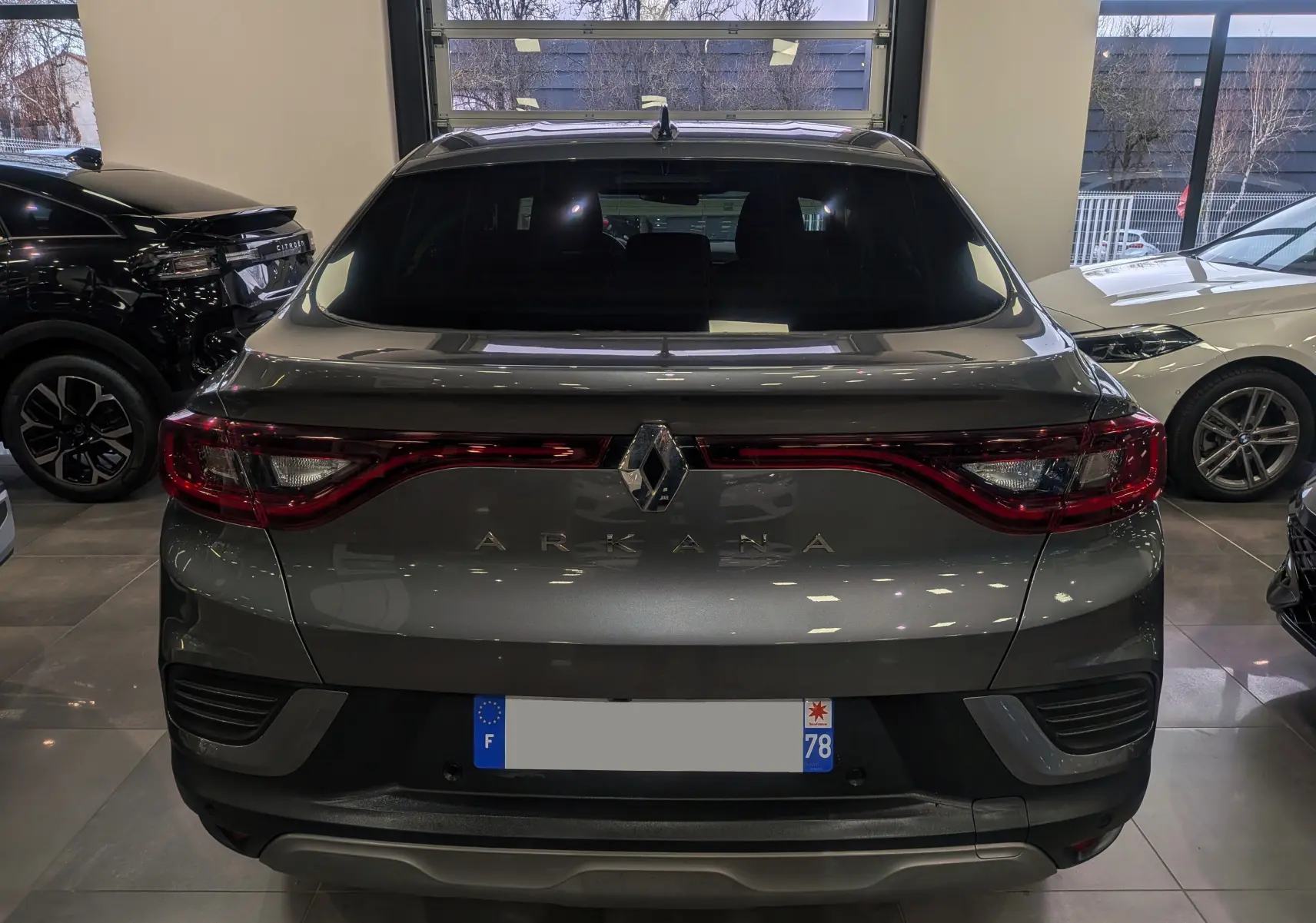 Vue arrière d'un Renault Arkana gris métal 2022 dans un showroom, avec feux arrière allongés et logo central lumineux.