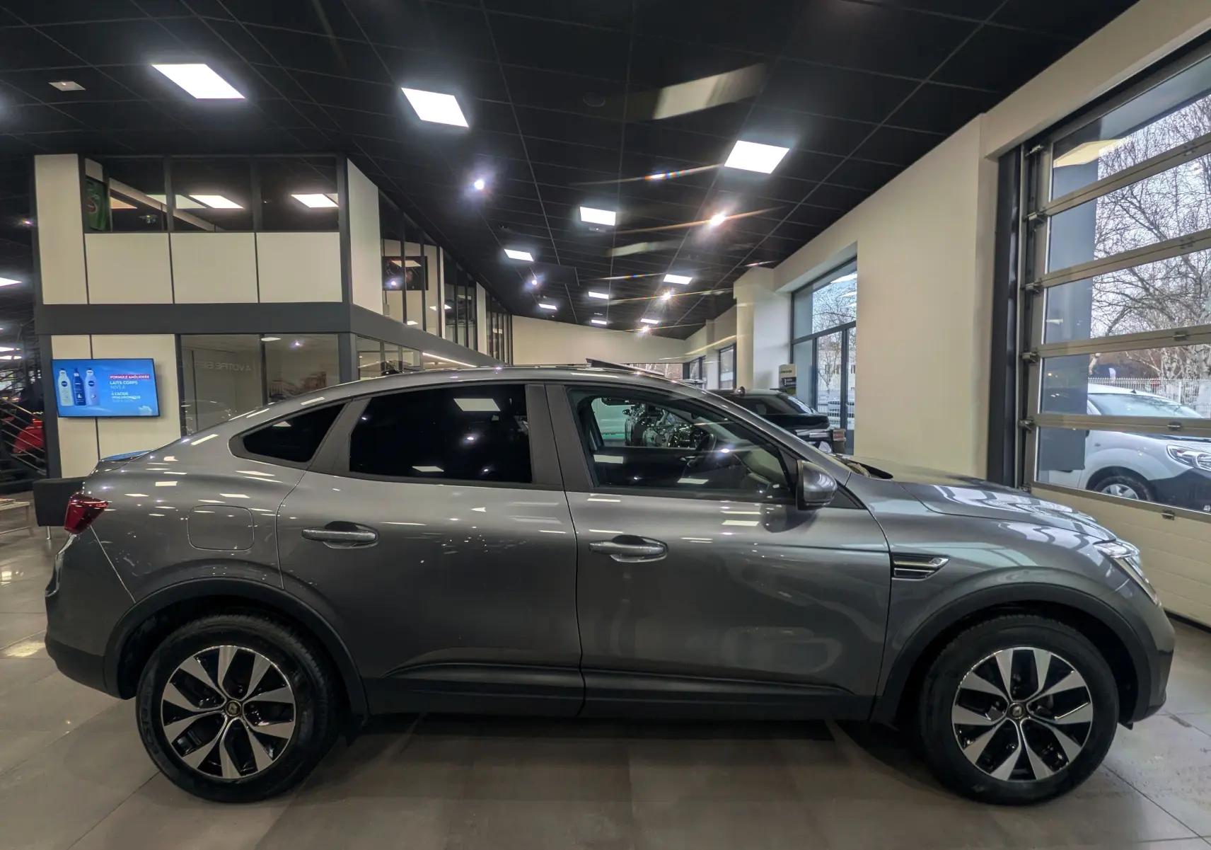 Vue de profil côté gauche d'un Renault Arkana gris métal 2022 en hybride essence, avec jantes bi-ton et vitres teintées.