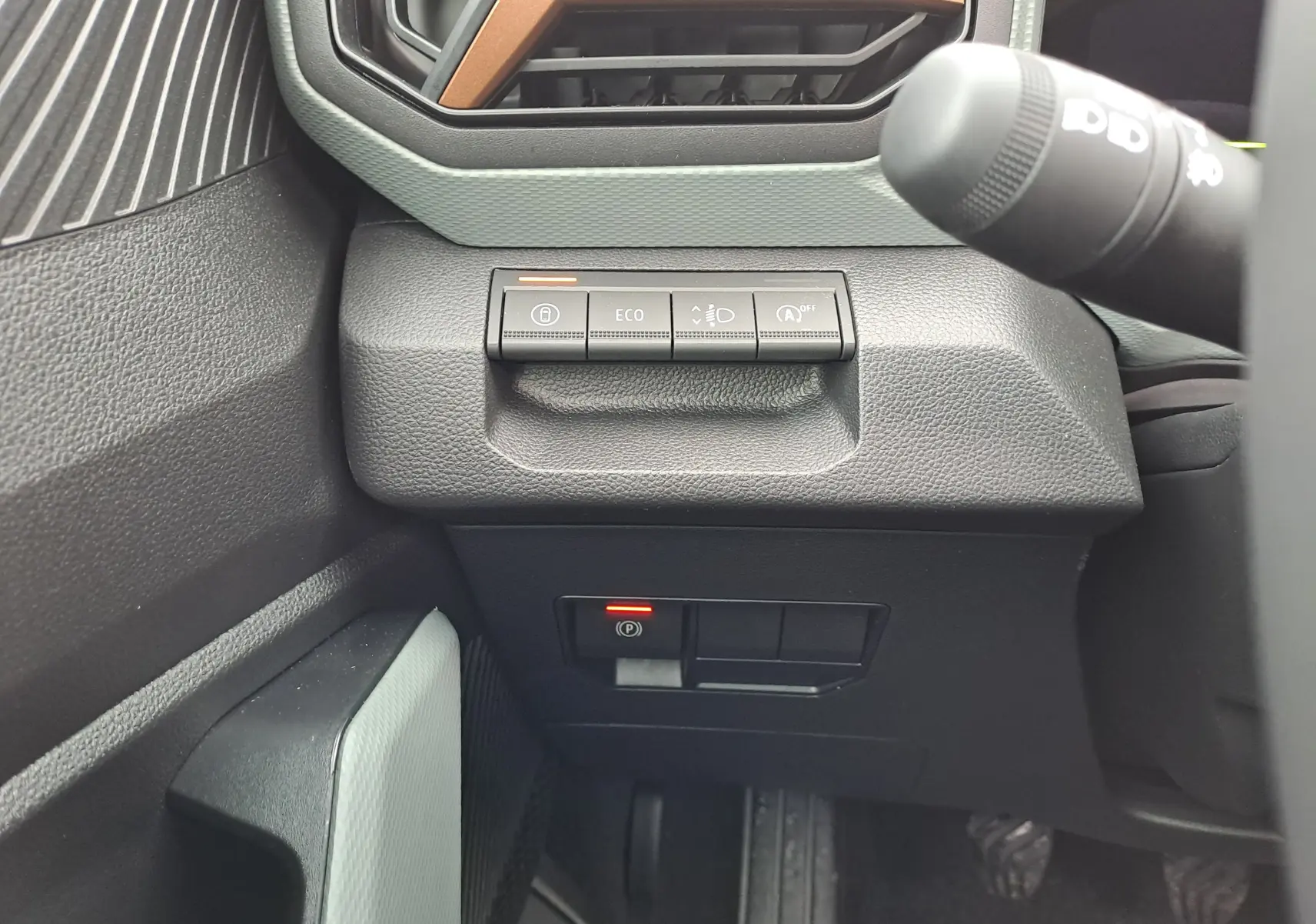 Détail intérieur du tableau de bord côté gauche du Dacia Bigster noir nacré, avec boutons de contrôle et frein à main électronique.