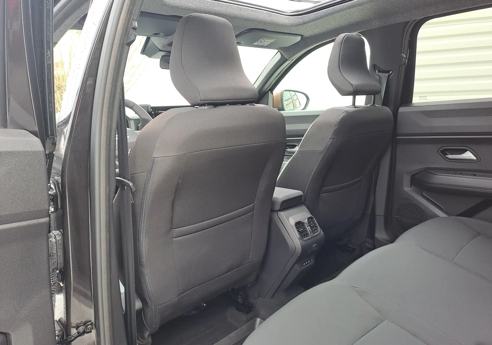 Vue intérieure arrière du Dacia Bigster noir nacré, montrant les sièges avant en tissu gris et les aérateurs centraux.
