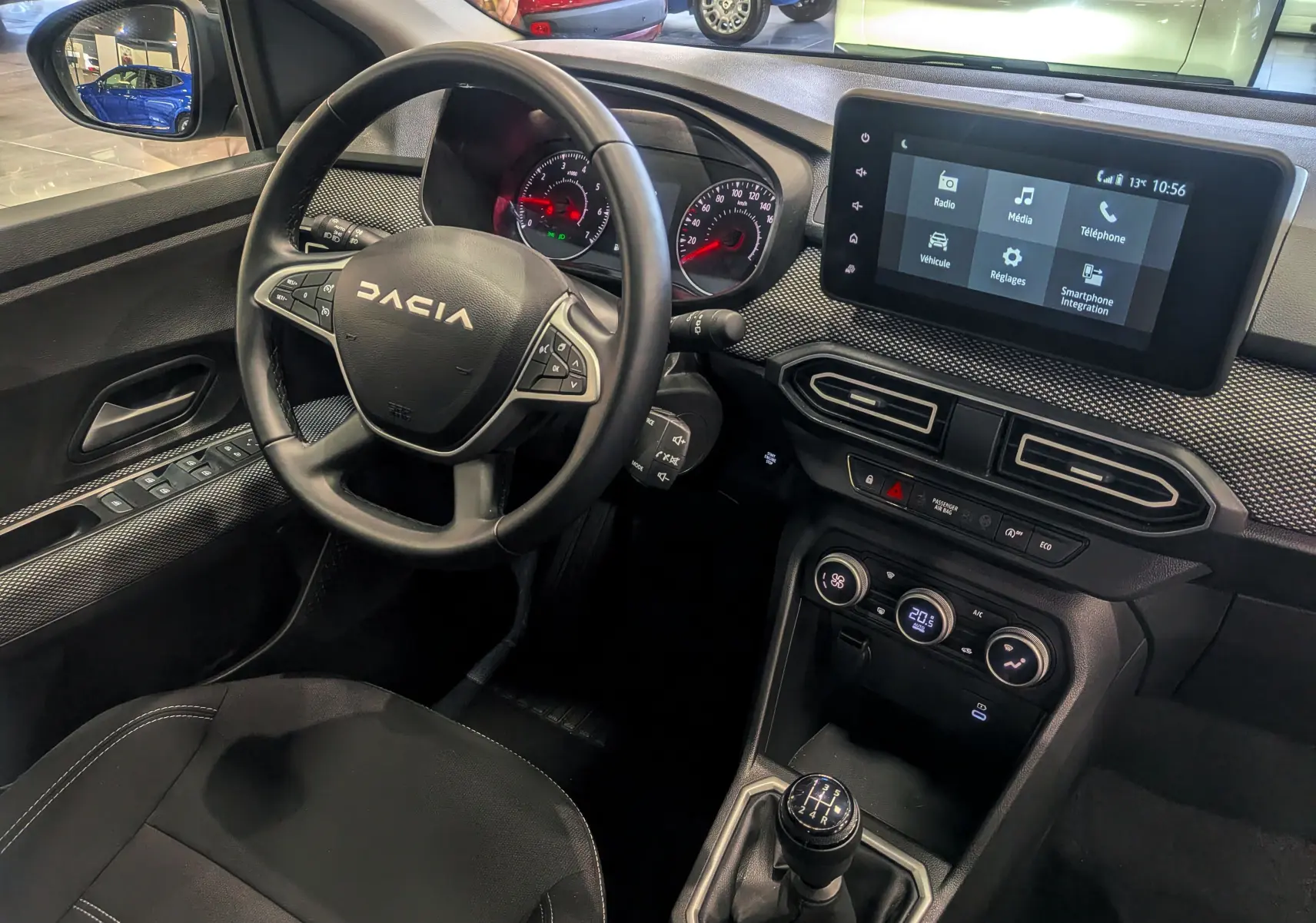 Vue intérieure côté conducteur du tableau de bord et volant DACIA Sandero TCe 90 gris, avec écran tactile et levier de vitesse manuel.