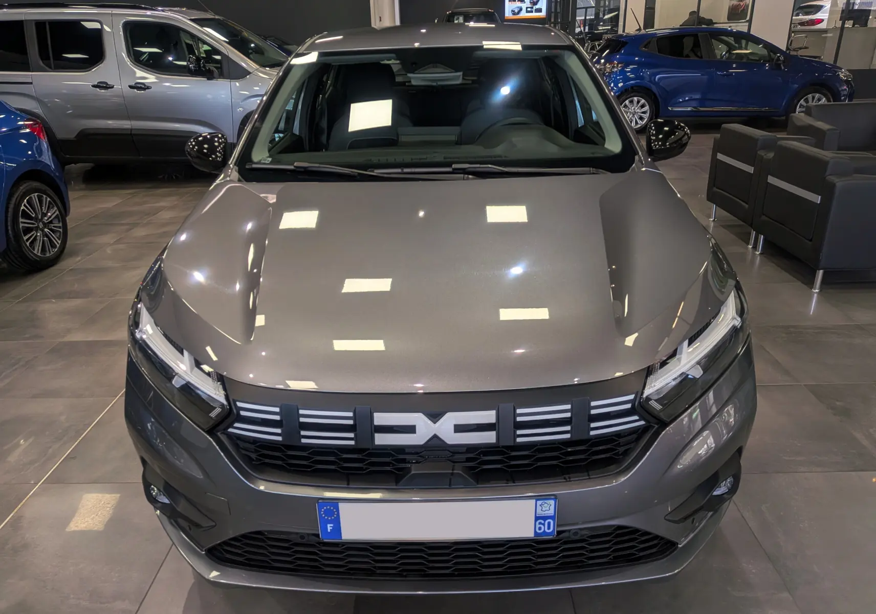 Vue de face d'une Dacia Sandero TCe 90 gris schiste, avec calandre noire et phares LED, en showroom intérieur.