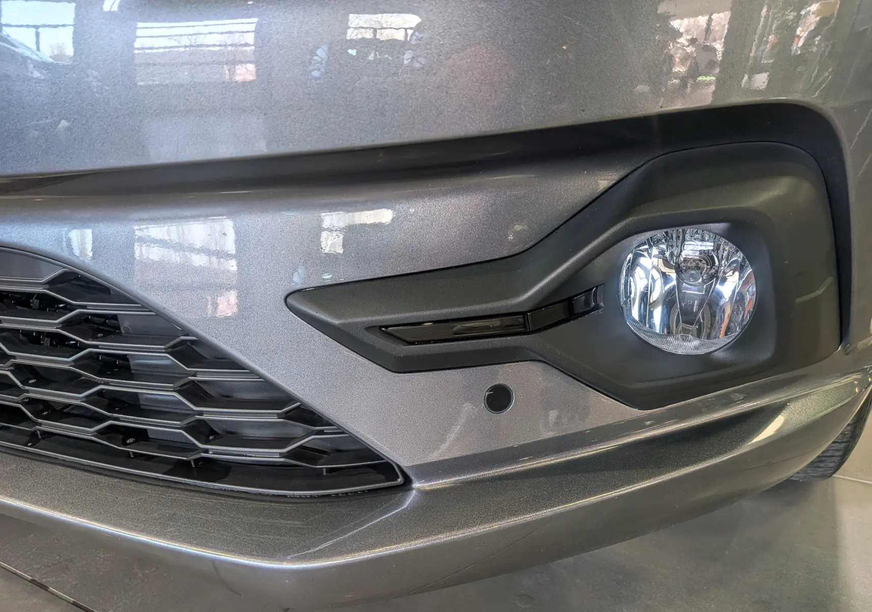 Gros plan sur le pare-chocs avant droit gris schiste du Dacia Sandero TCe 90 CH JOURNEY avec antibrouillard et calandre noire.