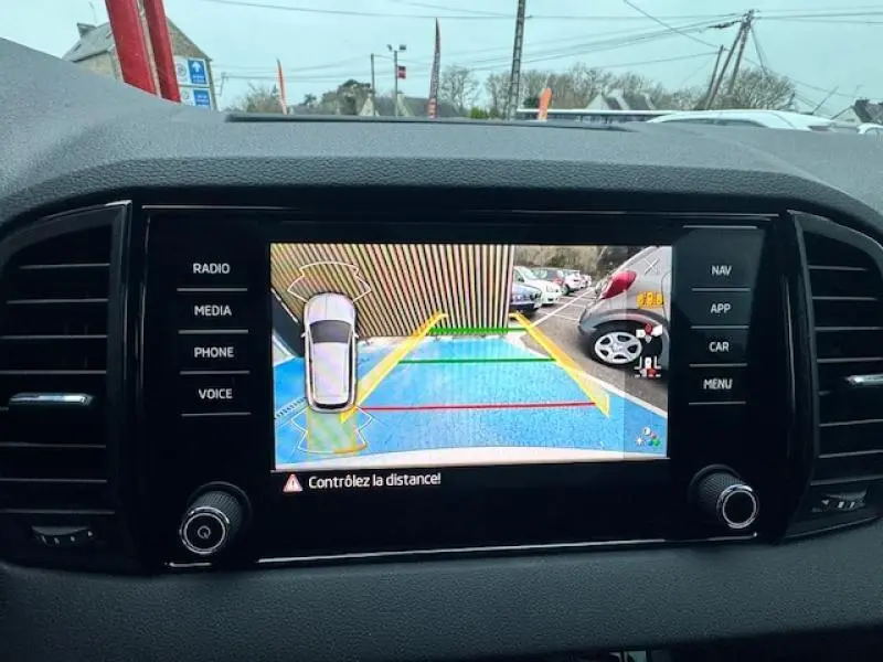 Écran tactile intérieur montrant la caméra de recul d'une Skoda Karoq gris diamant, vue arrière avec lignes de guidage colorées.