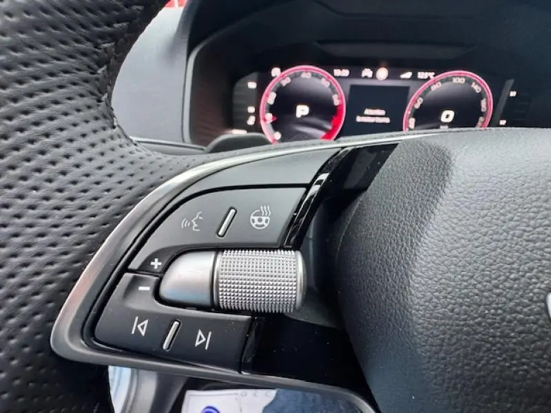 Gros plan sur les commandes du volant cuir noir perforé d’un Skoda Karoq 2025 avec tableau de bord numérique en arrière-plan.