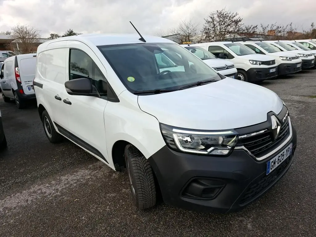 Renault Kangoo blanc en 3/4 avant droit, avec pare-chocs noir et calandre distinctive, stationné en extérieur.