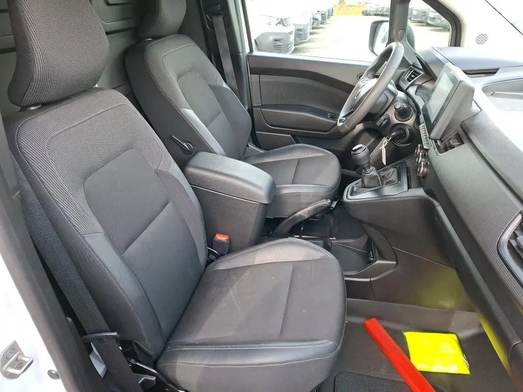 Vue intérieure côté conducteur du Renault Kangoo blanc 2023, montrant les sièges noirs et la console avec boîte manuelle.