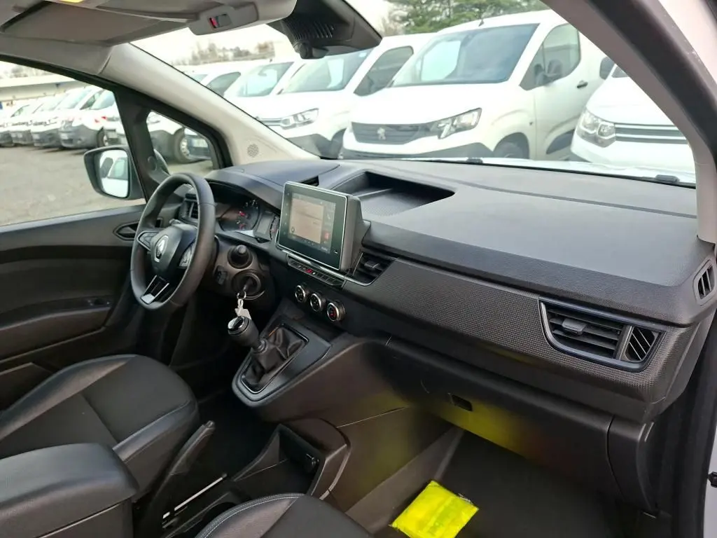Vue intérieure côté conducteur du Renault Kangoo blanc 2023, mettant en valeur le tableau de bord avec écran tactile et boîte manuelle.