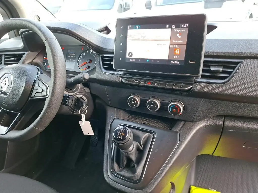 Vue intérieure du tableau de bord et levier de vitesses manuel du Renault Kangoo blanc 2023 avec écran tactile et commandes climatisation.
