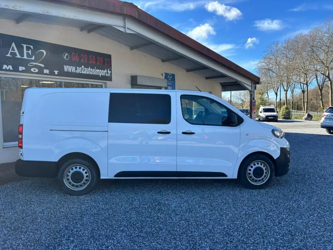 Vue de profil côté gauche du Peugeot Expert Fourgon blanc, version Long 2018, stationné devant un bâtiment.
