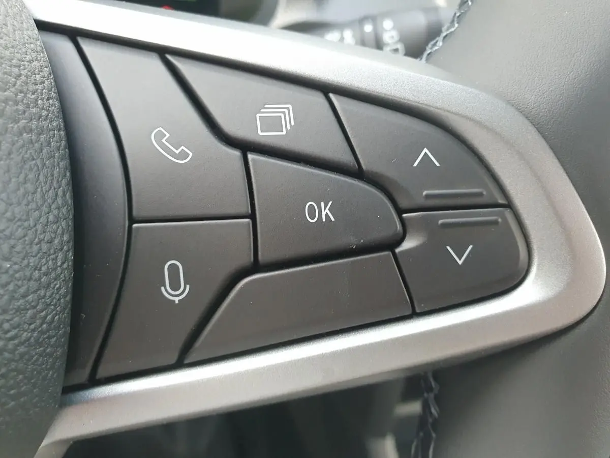 Gros plan sur les boutons de commande au volant du Dacia Duster 2026, finition gris schiste, avec commandes vocales et navigation.