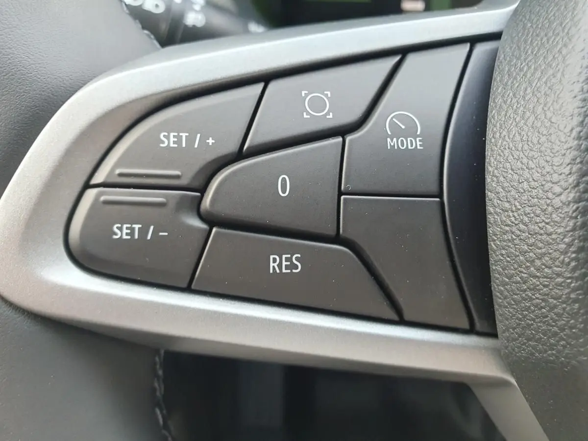 Gros plan sur les commandes noires du volant du Dacia Duster 2026, avec cadre argenté autour des boutons.