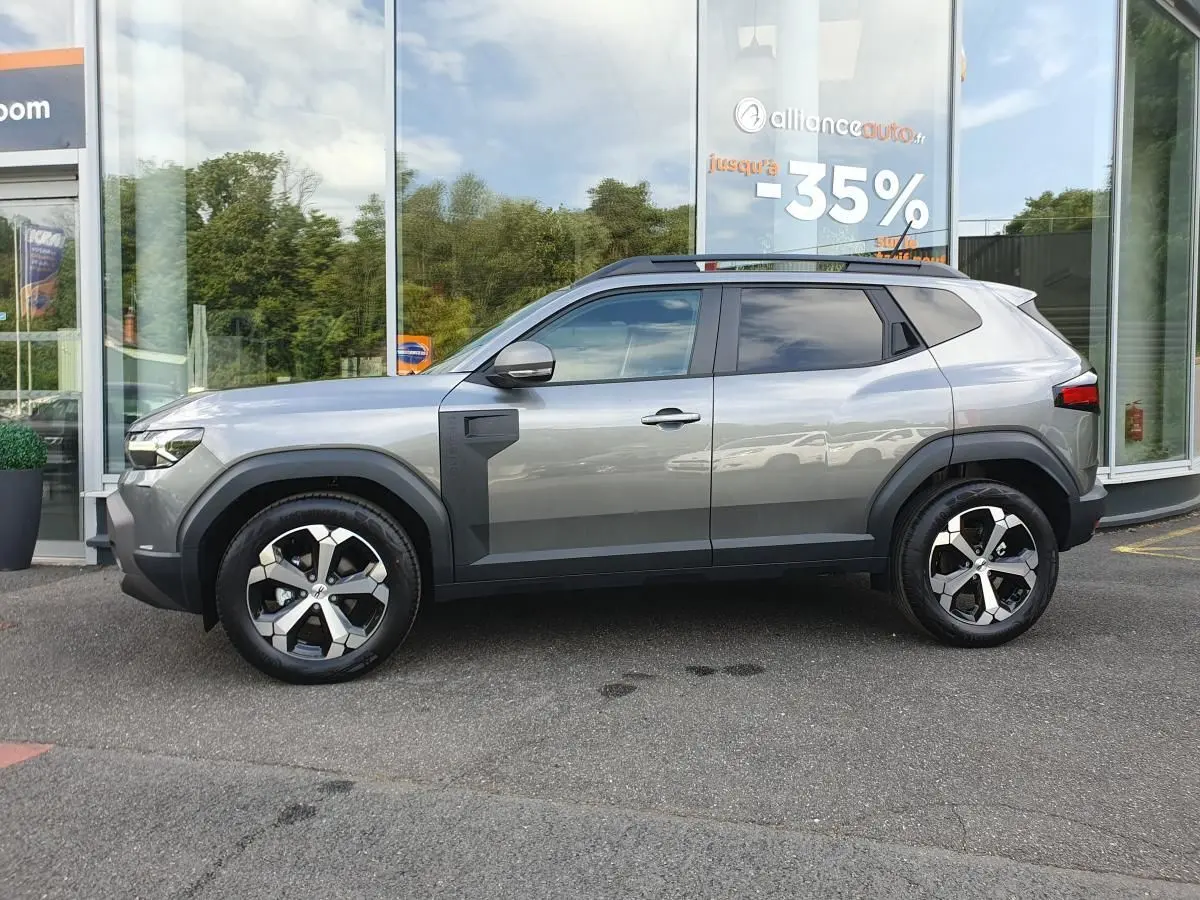 Vue de profil côté gauche d’un Dacia Duster 2026 gris schiste avec jantes alliage 18 pouces et barres de toit.