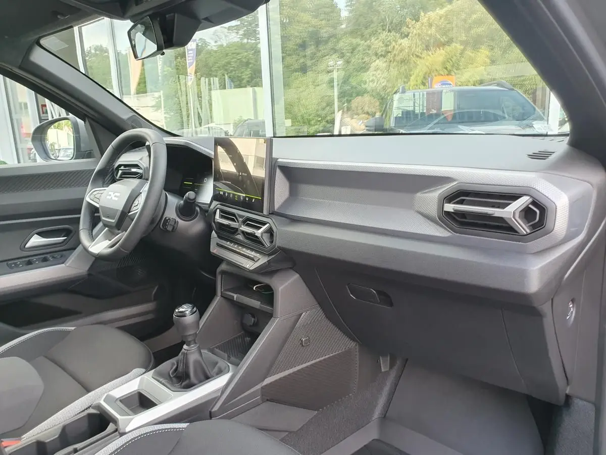 Vue intérieure côté passager du tableau de bord gris et console centrale avec écran tactile du Dacia Duster 2026.
