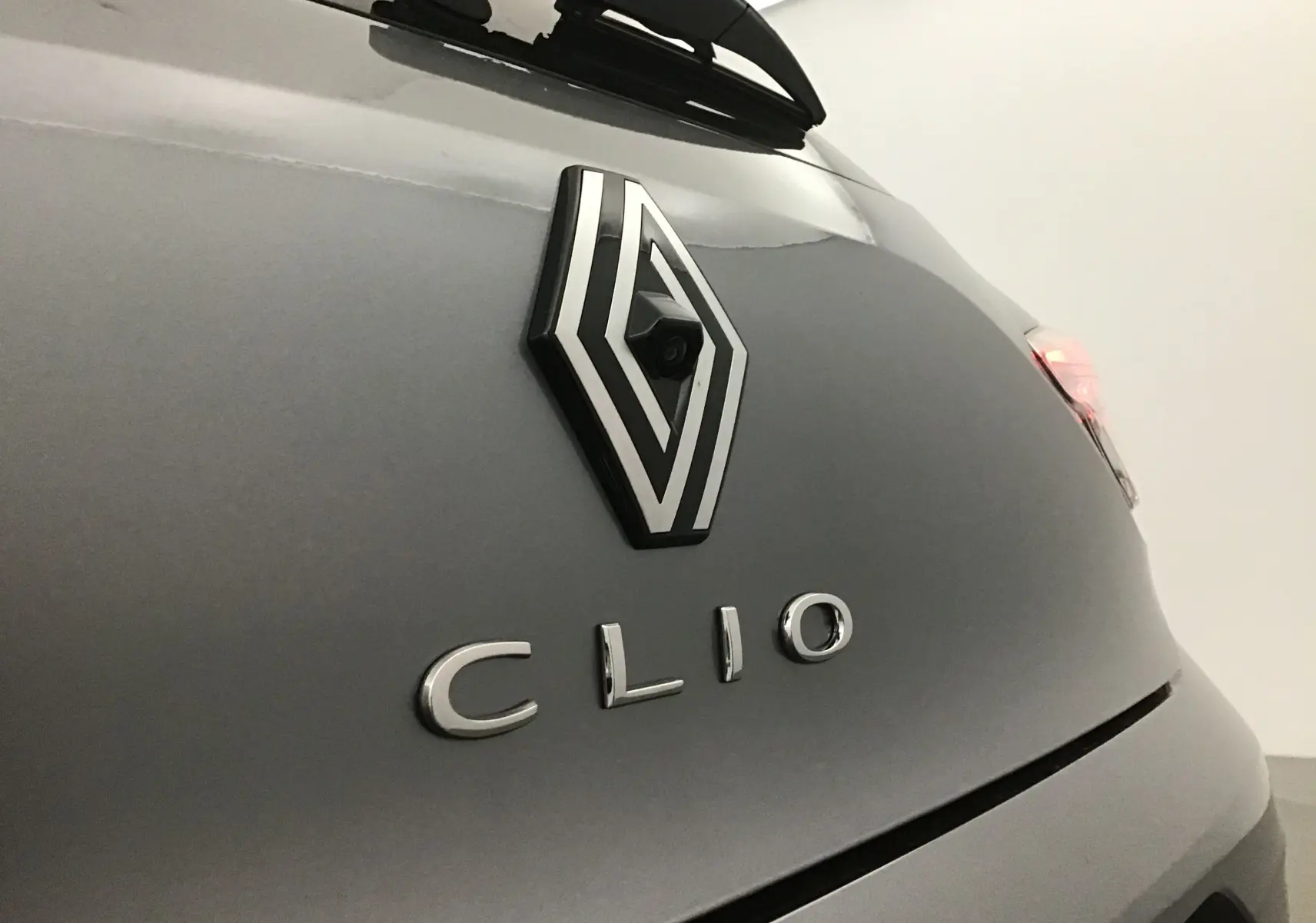Gros plan sur l'arrière gris schiste d'une Renault Clio V avec logo et caméra de recul intégrée visible.
