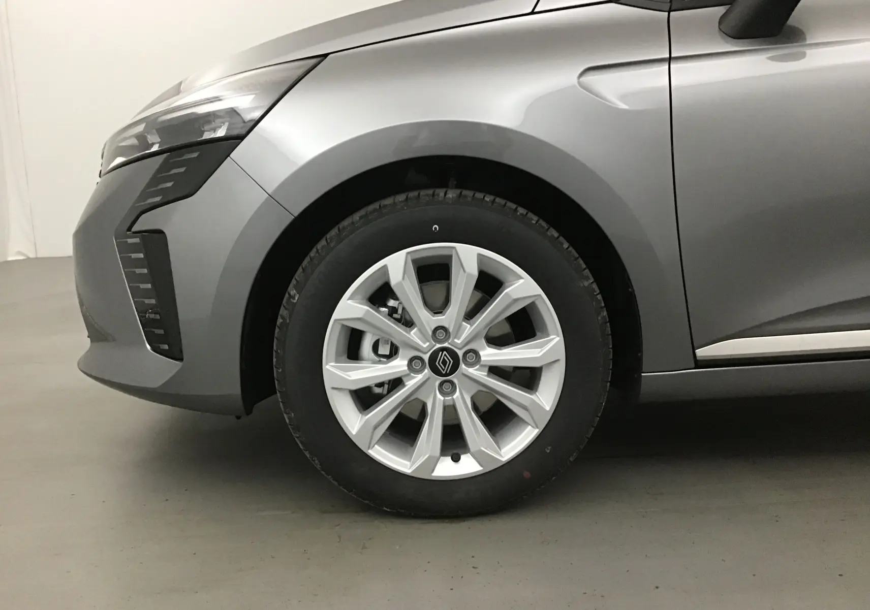 Gros plan sur la roue avant gauche d'une Renault Clio V gris schiste, avec jante alliage et partie avant du véhicule visible.