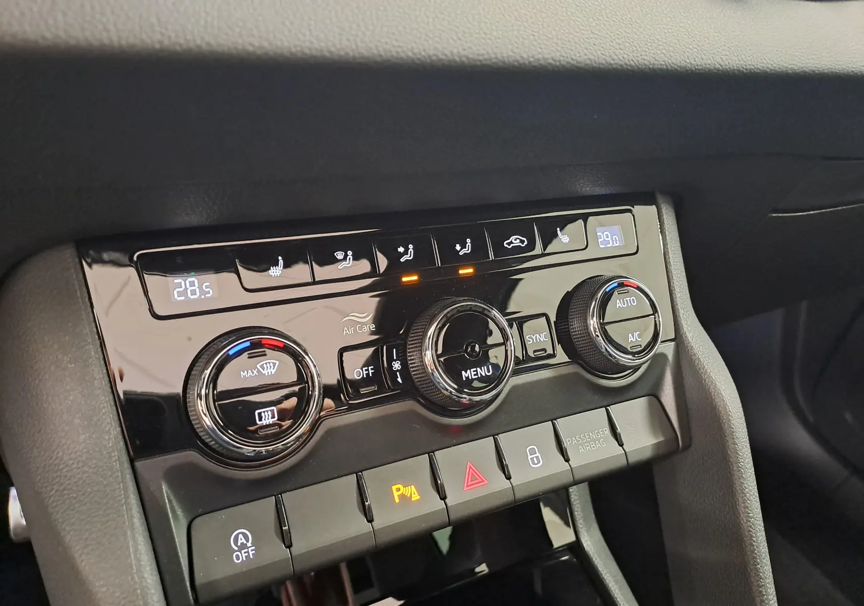 Gros plan sur la console centrale du Skoda Karoq Bleu RS 2025, montrant les commandes de climatisation tri-zone et les voyants allumés.