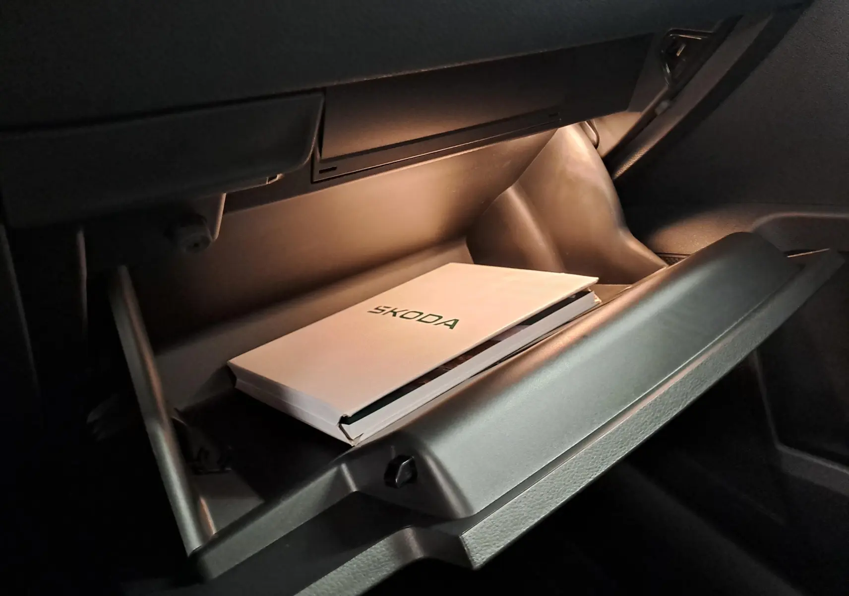 Gant de boîte à gants ouvert avec manuel SKODA à l'intérieur, intérieur sombre du SKODA KAROQ 2025.