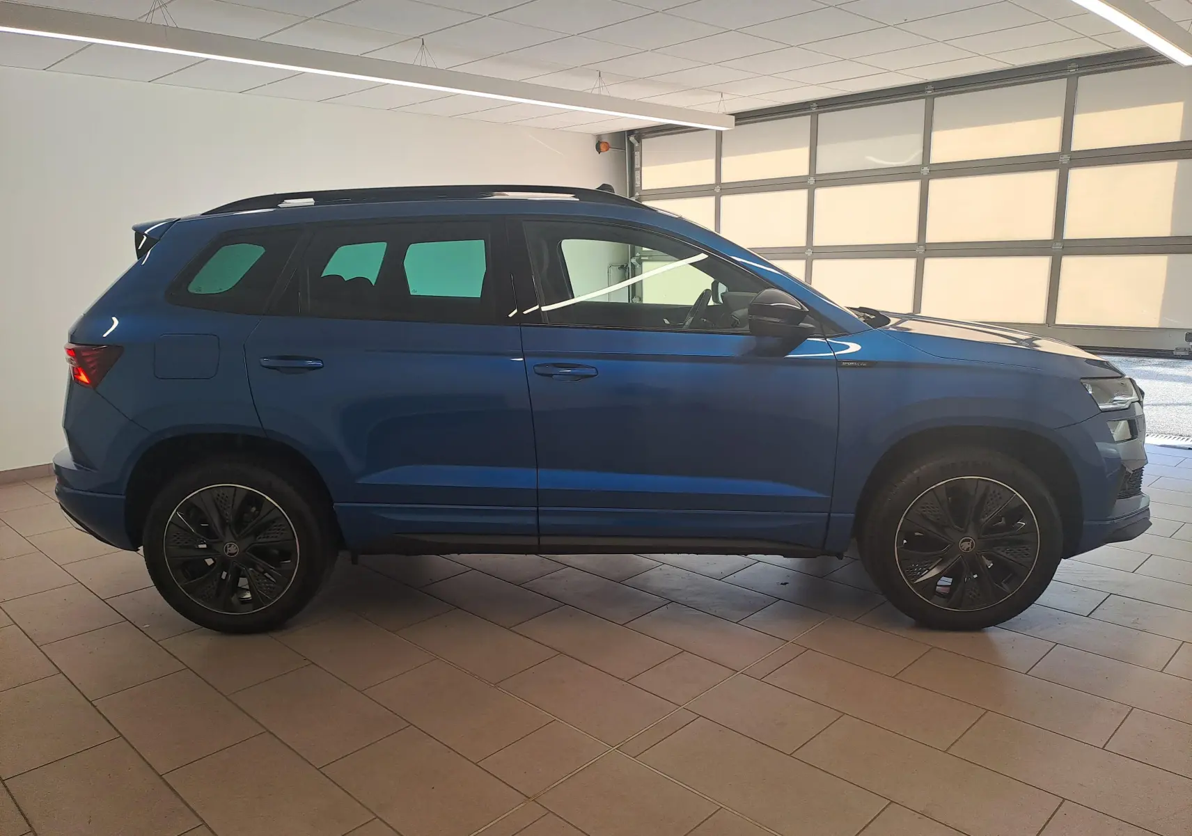 Vue de profil côté gauche du Skoda Karoq 2025 en Bleu RS avec toit panoramique ouvrant et jantes noires sport.