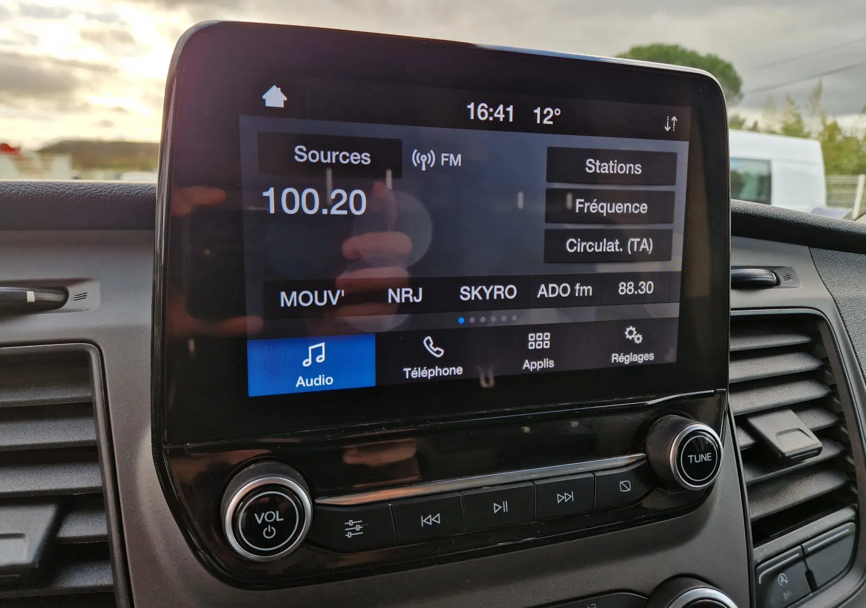 Vue rapprochée de l’écran tactile multimédia du Ford Transit Custom blanc, affichant la radio FM à 100.20 MHz.