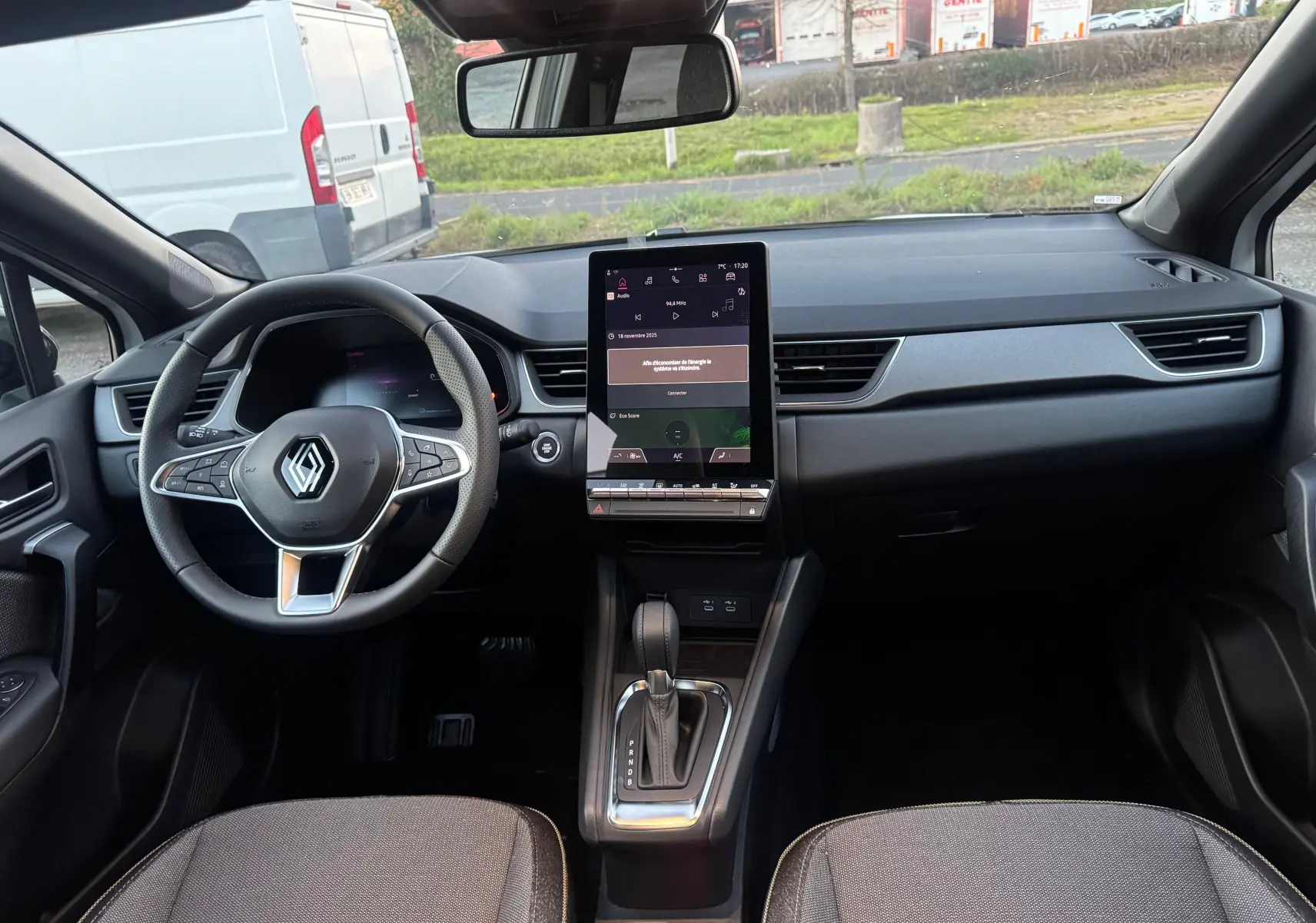 Vue intérieure avant du Renault Captur 2025 E-Tech, tableau de bord noir avec écran tactile vertical et volant multifonction.