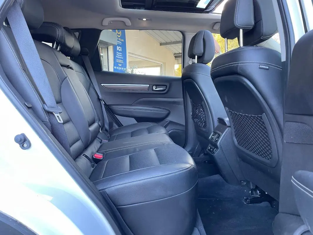 Vue intérieure côté arrière gauche du Renault Koleos blanc 2019, montrant les sièges en cuir noir et le toit ouvrant panoramique.