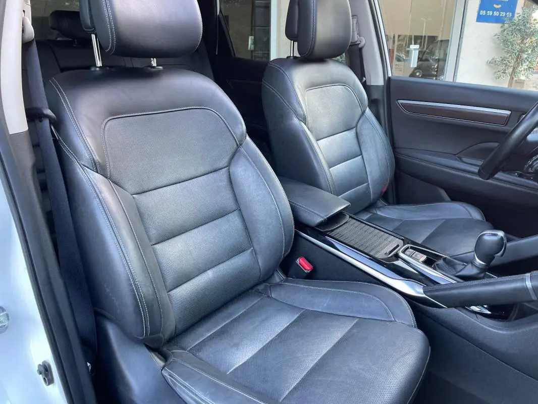 Vue intérieure des sièges avant en cuir noir du Renault Koleos blanc 2019, avec accoudoir central et console centrale visible.