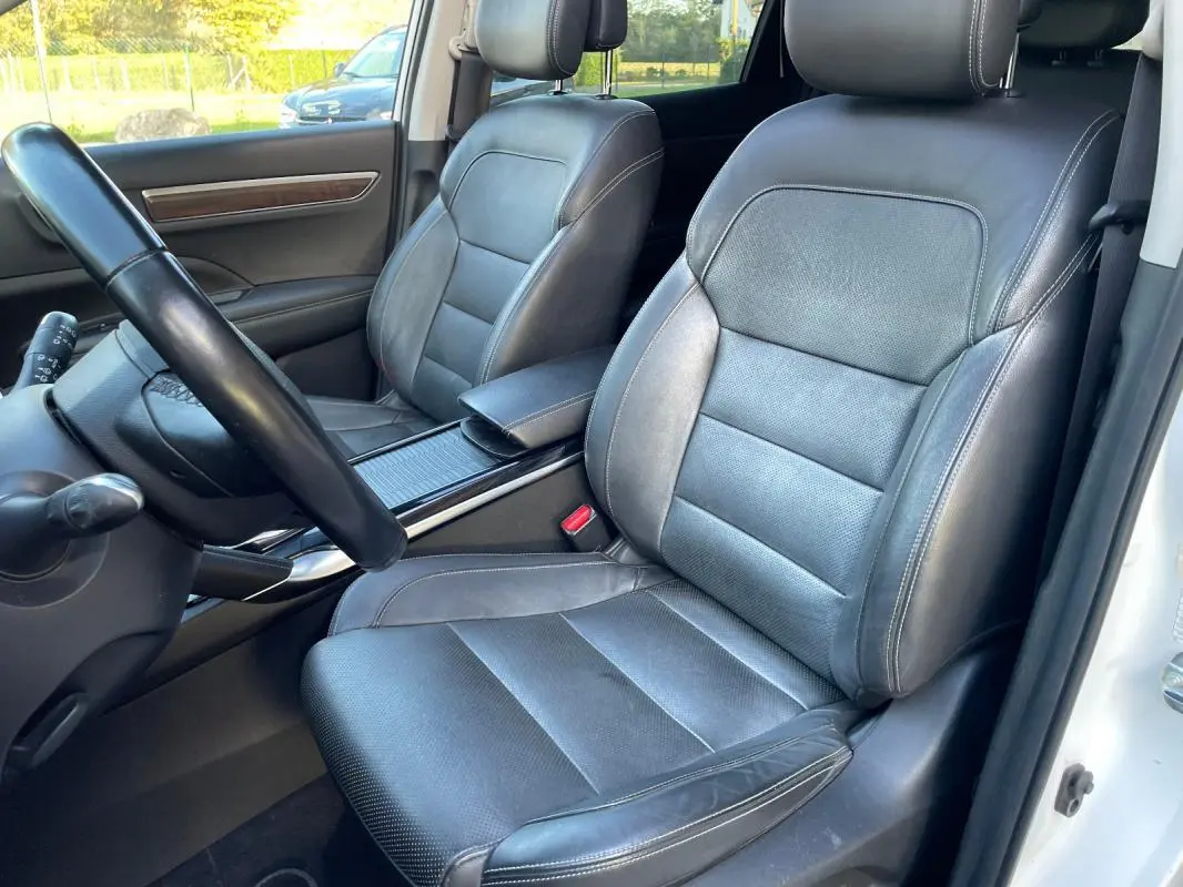 Vue intérieure côté conducteur du Renault Koleos blanc 2019, sièges cuir noirs avec accoudoir central visible.