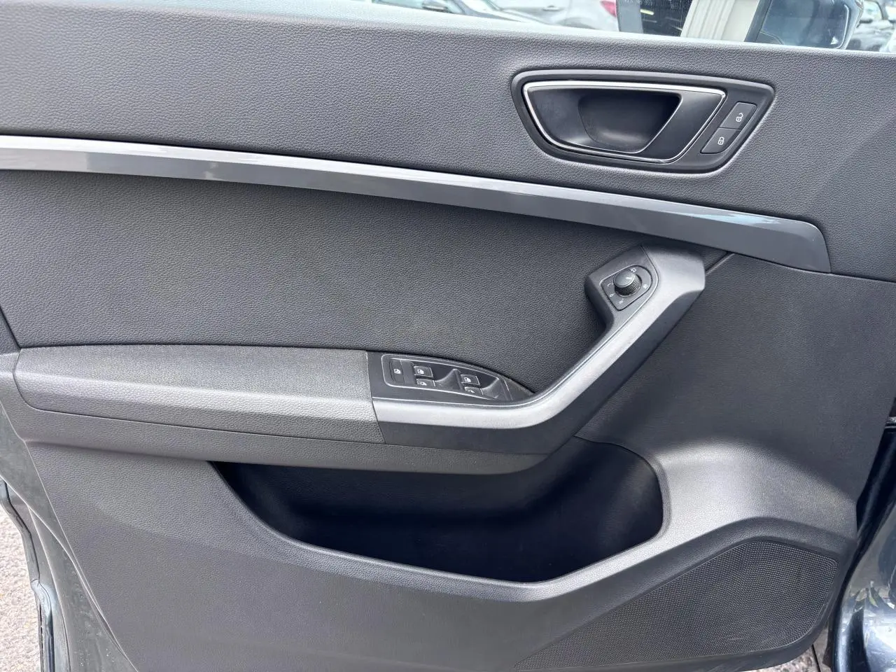 Vue intérieure côté gauche de la porte avant d'une SEAT Ateca gris foncé avec commandes électriques et poignée intégrée.
