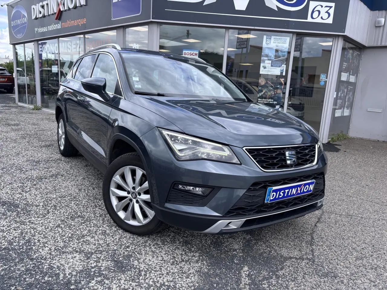 SEAT Ateca gris foncé en vue 3/4 avant droit, avec calandre chromée et jantes alliage 17 pouces visibles.