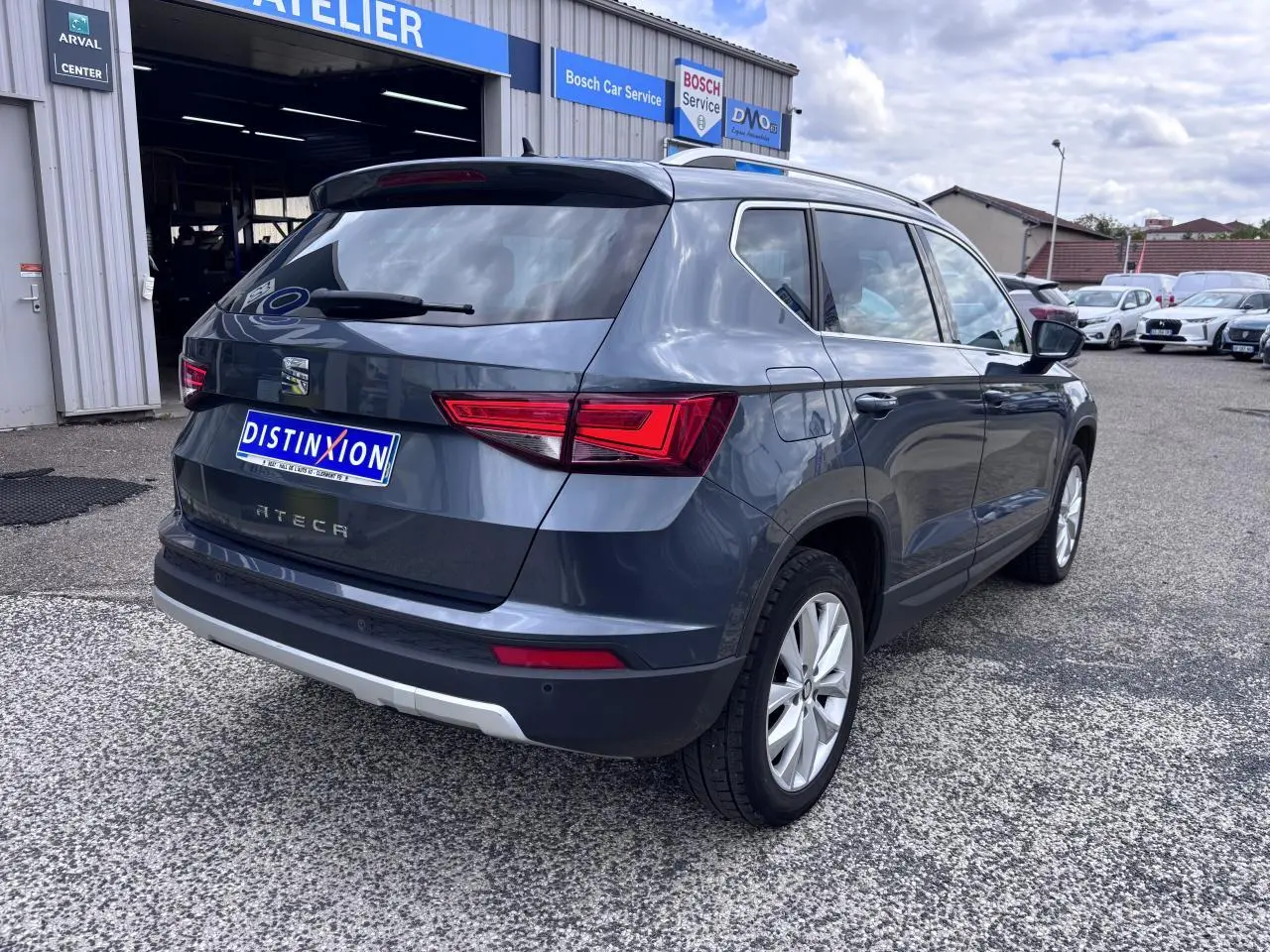 Vue 3/4 arrière droite d’un SEAT Ateca gris foncé avec feux LED et jantes alliage 17 pouces, stationné devant un atelier.