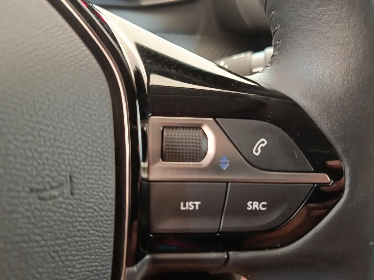 Gros plan sur les commandes noires du volant cuir multifonctions côté gauche d’une Peugeot 208 PureTech 100 S&S Style 2022.