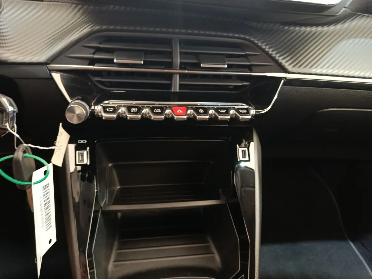 Vue rapprochée du tableau de bord noir de la Peugeot 208 PureTech 100, avec commandes et ports USB visibles.