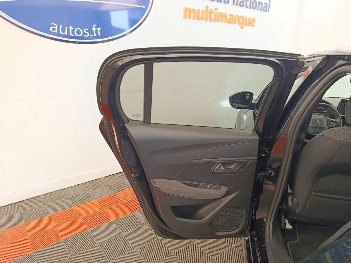 Vue intérieure de la porte arrière gauche ouverte d’une Peugeot 208 noire, montrant les détails du panneau de porte.