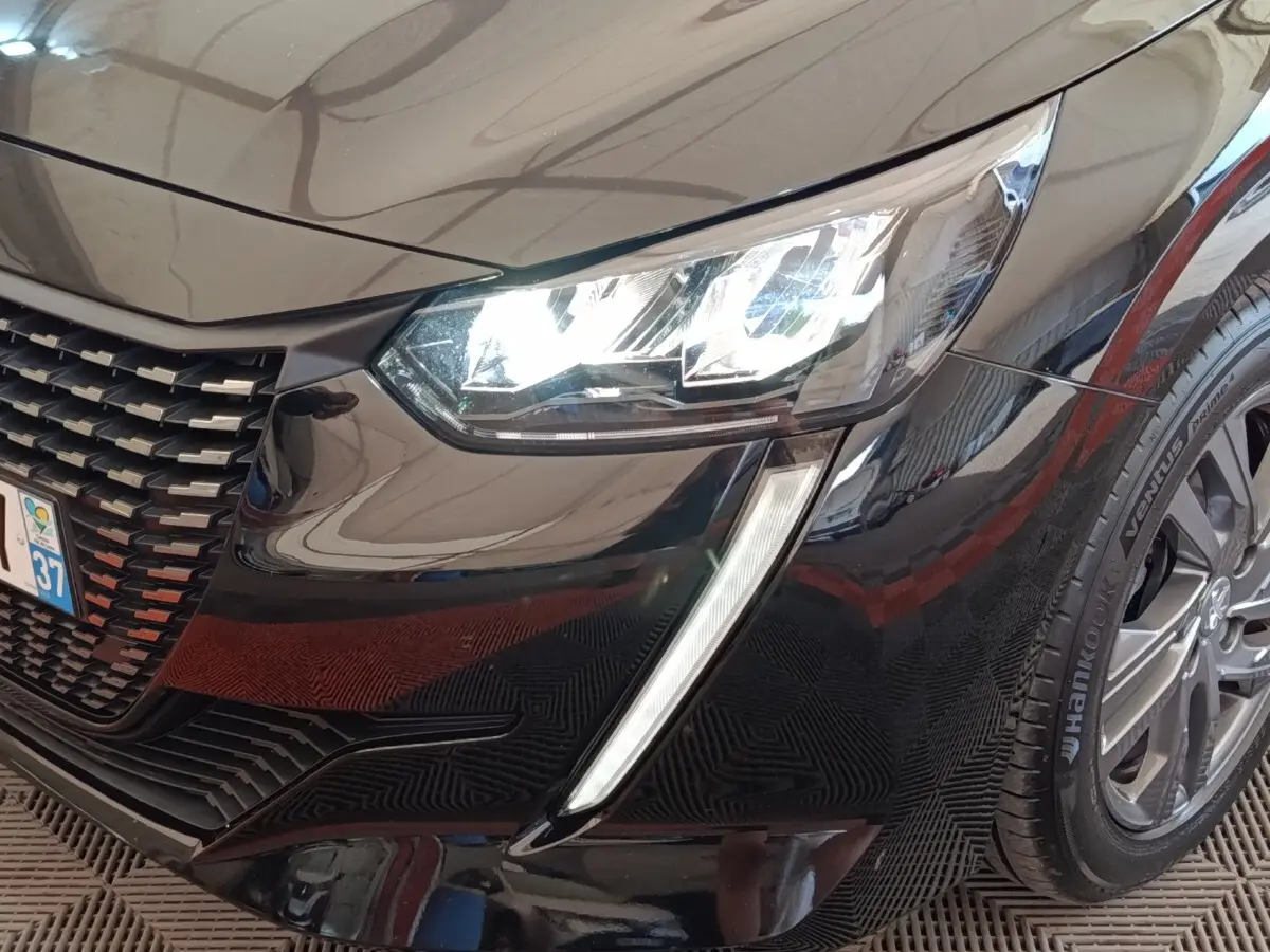 Gros plan sur l'avant droit noir brillant d'une Peugeot 208 2022, mettant en valeur le phare LED et la calandre distinctive.