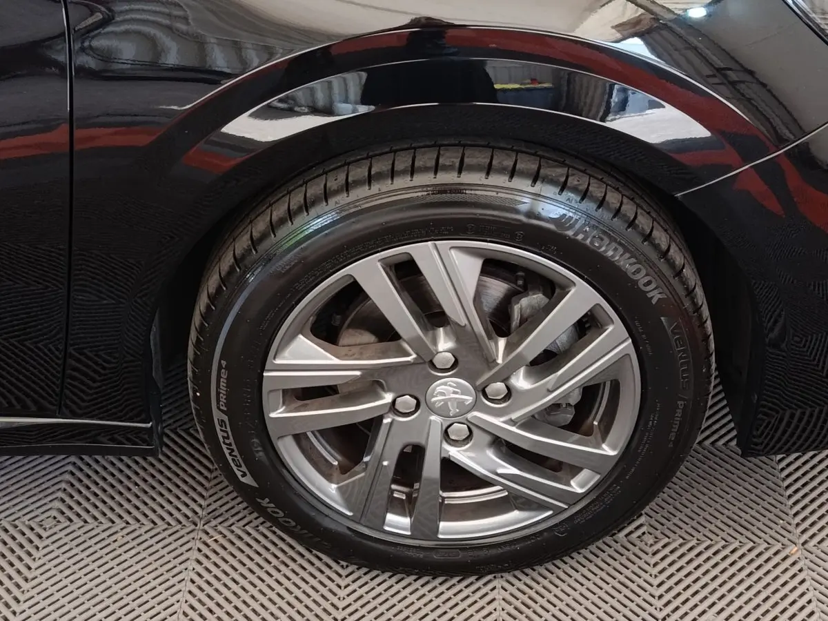 Gros plan sur la roue arrière droite d’une Peugeot 208 noire, jante alliage et pneu Hankook visibles.
