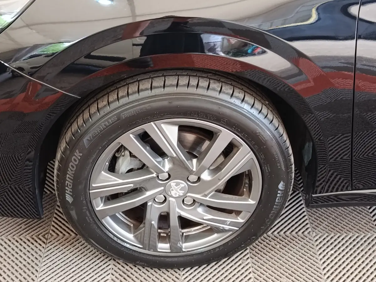 Gros plan sur la roue arrière droite d'une Peugeot 208 noire 2022 avec jante alliage et logo Peugeot visible.