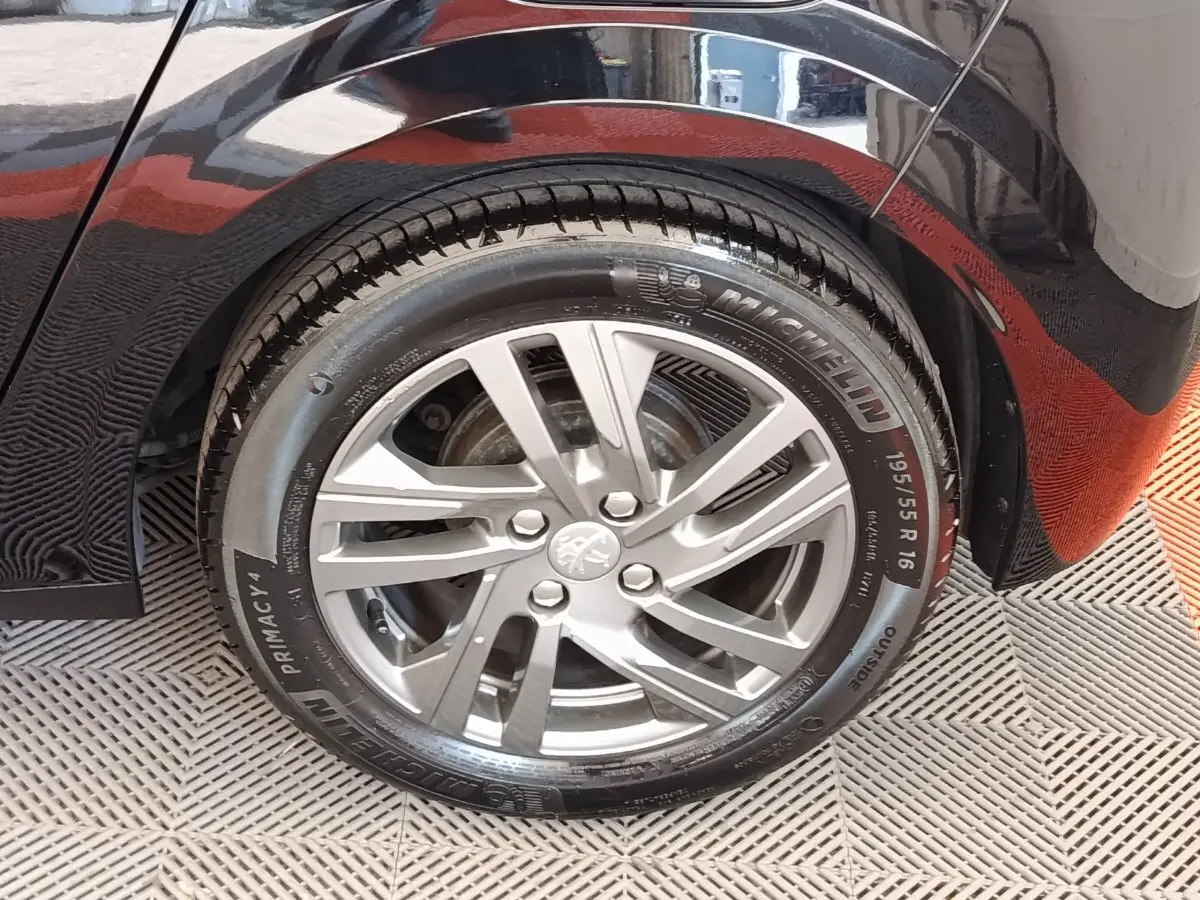 Gros plan sur la roue arrière droite d'une Peugeot 208 noire, mettant en valeur la jante alliage et le pneu Michelin.