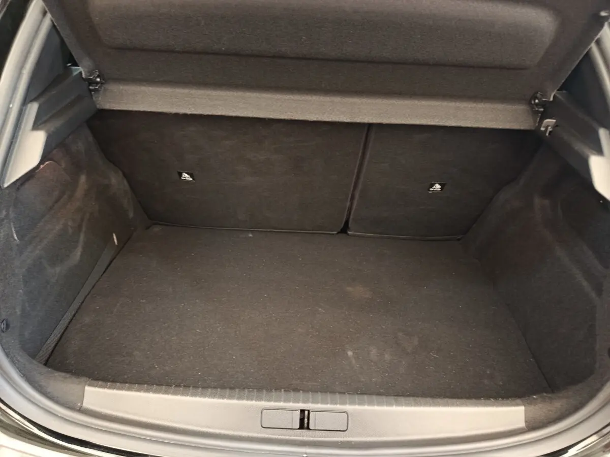 Coffre ouvert de la Peugeot 208 PureTech 100 S&S Style noir, montrant l’espace de chargement vide et la banquette arrière rabattable.