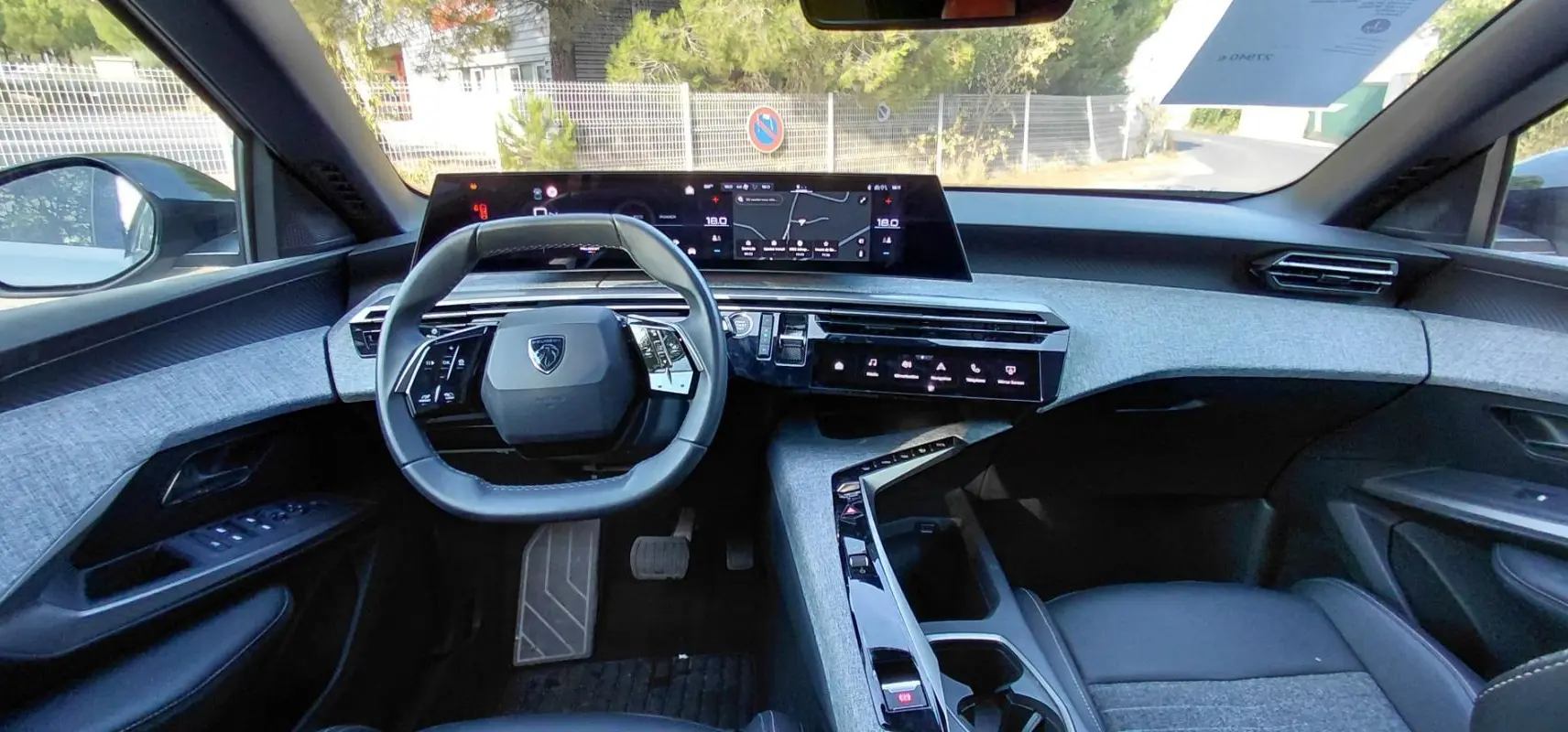 Intérieur du Peugeot 5008 Hybrid 2025 vu de face, tableau de bord moderne avec écran large et volant compact gris.