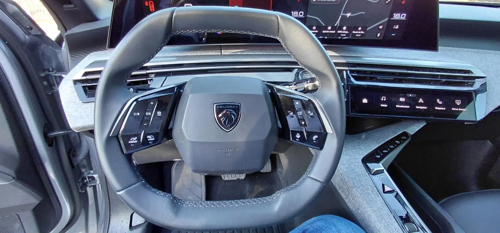 Vue rapprochée du volant cuir noir du Peugeot 5008 Hybrid 2025 avec tableau de bord numérique et commandes tactiles.