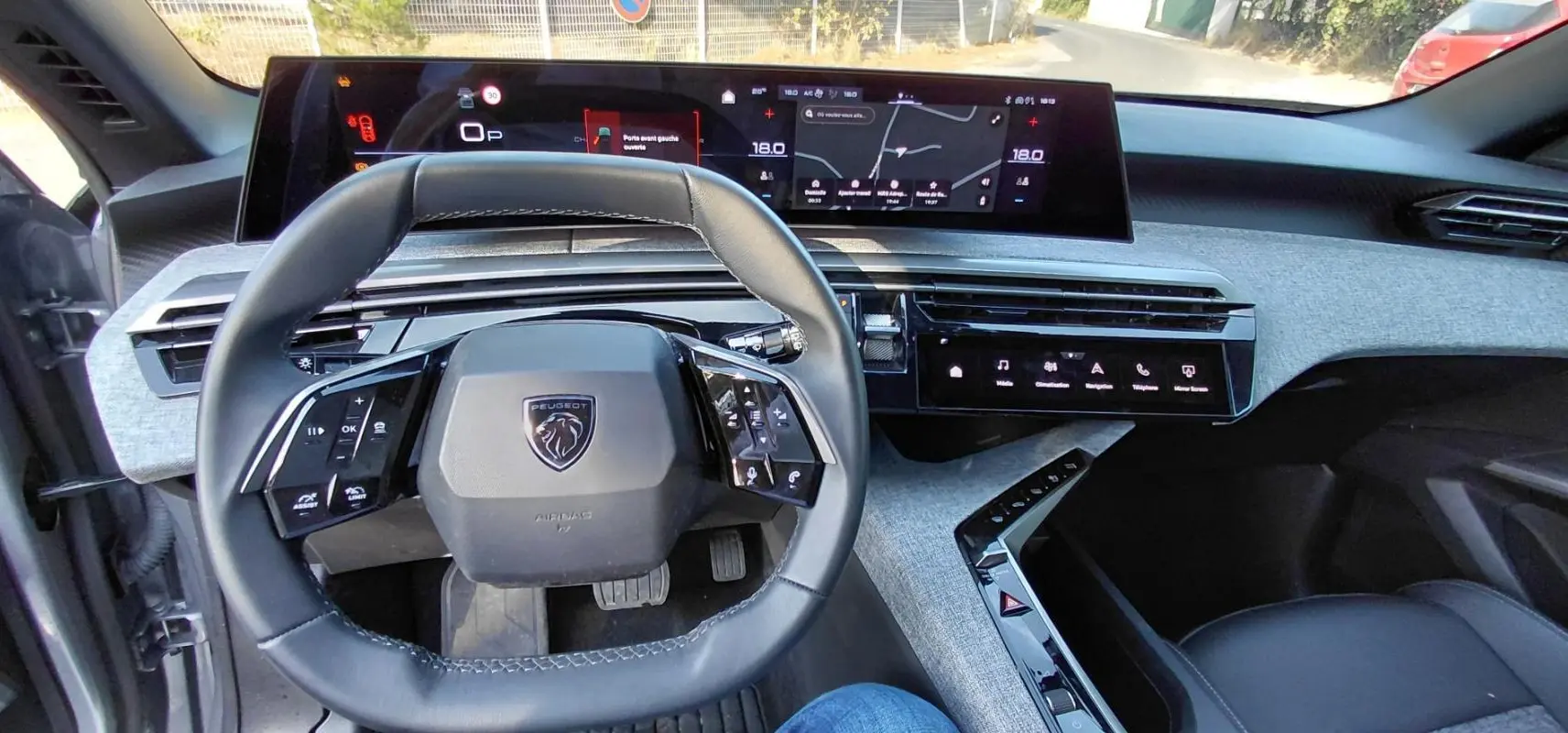 Vue intérieure du poste de conduite du Peugeot 5008 Hybrid gris 2025, avec volant compact et double écran numérique.