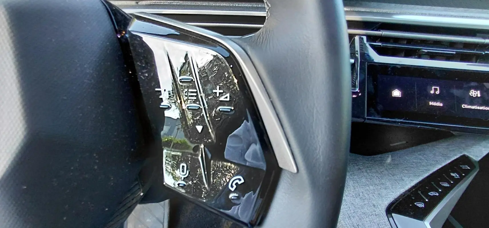 Gros plan sur les commandes au volant côté gauche du Peugeot 5008 gris Hybrid 2025, avec écran tactile en arrière-plan.