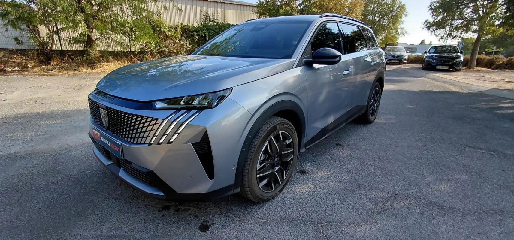 Peugeot 5008 Hybrid gris en 3/4 avant droit, avec calandre distinctive et jantes noires modernes.
