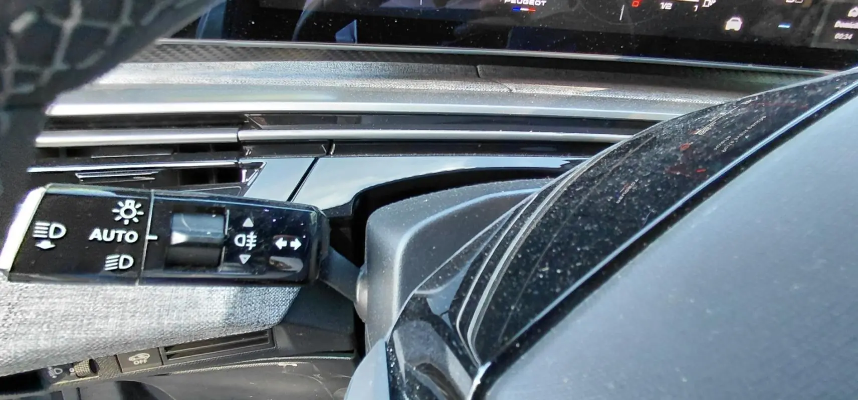Détail intérieur du Peugeot 5008 Hybrid 2025 montrant la commande des feux et une partie du tableau de bord noir brillant.