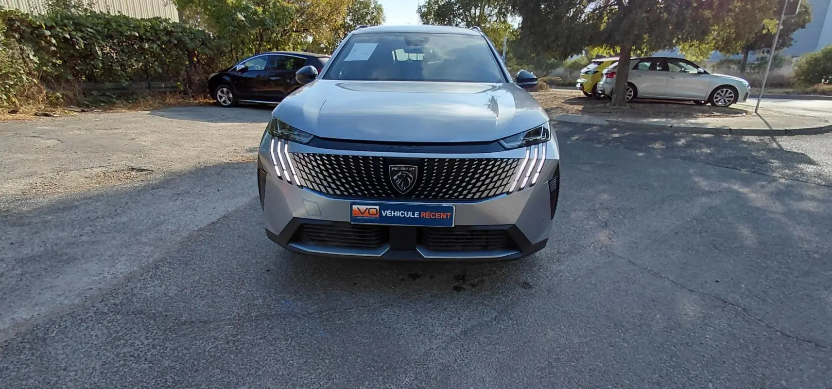 Peugeot 5008 Hybrid gris 2025 vu de face, avec calandre noire distinctive et feux LED en griffes allumés.